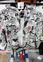 Front and partial back view of the vintage comic-themed sweatshirt with hood shown on a hanger. Zipper partially undone revealing white shirt underneath. Comic books stacked beneath.