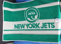 Photo showing full view of the green and white New York Jets blanket featuring the team helmet logo and text.