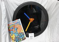 Front view of the Superman wall clock next to the comic book showing the clock hands and Superman logo
