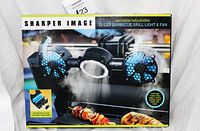 Box front showing product image of the Sharper Image portable adjustable BBQ grill light and fan with branding and features.