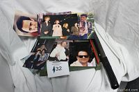 Photo showing a pile of vintage celebrity photographs spread on a white surface with a box underneath and auction lot tag 432 visible.