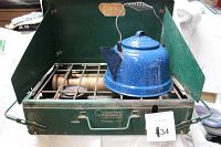Coleman camp stove with blue speckled kettle placed on top, showing side windshields and burner area.