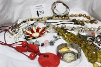 Photo showing a variety of vintage costume jewelry items including necklaces, two watches, bracelets, a flower brooch, and earrings placed on white fabric background.