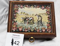 Closed jewelry box showing the wooden frame and vintage tapestry lid with children and floral border
