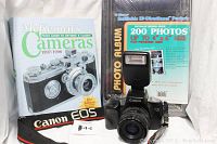 Canon EOS 750 camera with flash, Canon EOS strap, McKeown's Cameras 1997/1998 book, and new photo album in original packaging.