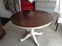 Round wood pedestal table showing dark wood top with visible edge wear and white painted base with light spotting.