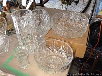 Five crystal pieces grouped showing three vases of different sizes and two bowls, including one octagonal bowl raised on a cardboard box.