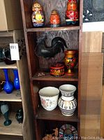 Shelf of assorted items including metal folk art rooster, Babushka dolls, vases, and other collectibles
