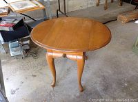 Photo showing the round solid wood drop leaf end table top and legs with some minor wear.