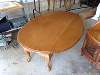 Photo showing top and side view of solid wood oval drop leaf coffee table with queen anne style legs and visible scratches.