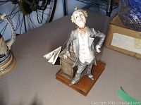 Side angle view of Capodimonte porcelain figure on wooden base, showing detailed face and attire, with certificate included nearby.