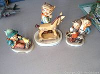 All three Hummel figurines displayed on a table showing the full view of each.