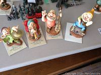 Four Disney Snow White and the Seven Dwarfs dwarfs figurines displayed on table, each standing on a labeled base, showing Dopey, Happy, Cheerful, and Zzzzzz characters.