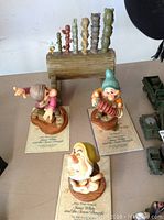 Overall view of three Disney Snow White and Seven Dwarfs character figurines with Certificates of Authenticity, and a pipe organ figure themed on the Seven Dwarfs