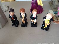 Four Royal Doulton ceramic figurines representing characters from Oliver Twist arranged on a table, showing full front view of each.