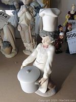 Porcelain chef figurine holding a large pot, angled to show front and side details, with other figurines blurred in background.