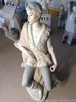 Full view of the Lladro figurine showing the young man in a textured tunic and leggings, kneeling with a scroll.