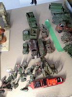 Overview of vintage military diecast vehicles and toy soldiers arranged on a table showing wear and some damage.