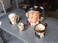 Four Royal Doulton Toby jugs displayed on a metal shelf, showing different angles and group arrangement.