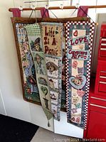 Photo shows four fabric tapestries hanging on wooden rods, including one large and three narrow small tapestries with various decorative motifs including bears, butterflies, hearts, and words.