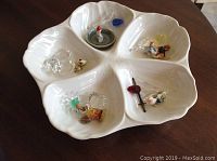 Overall view of white ceramic five-section dish containing small Swarovski crystal figures and ceramic figures.
