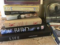 Stack of hardcover books showing titles including 'Nourishing Traditions,' 'Capitol Punishment,' 'Shanghai Girls,' 'Bird: The Definitive Visual Guide,' and 'Life by Lanting'