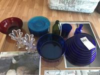 Overview of all glassware items including dark blue plates and bowls, teal green plates, blue and green glass bottles, clear candle holders, small red bowl.