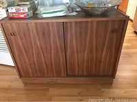 Front view of wooden cabinet showing sliding doors with recessed oval finger pull handles and wood grain finish.