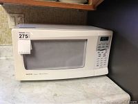 White Sanyo microwave oven on countertop with label 275 visible on the top left corner.