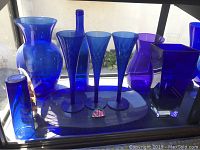 Blue glass vases, stemware, an oval platter and a fish-shaped figurine on a window sill with natural light.