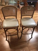 Pair of tall wood bar stools with vinyl seats and rattan woven backs on wood flooring in kitchen environment.