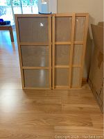 Six wooden triple photo frames leaning against a wall on wood flooring. Each frame has three vertical photo slots covered with glass or clear plastic.
