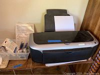 Full view of Epson Stylus Photo 2200 printer with paper loaded and plastic bin of ink cartridges and photo paper beside it.