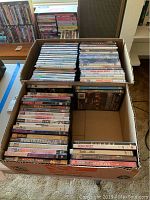 Top view of a box containing approximately 60 DVD movies arranged in rows inside a cardboard box.