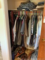 Closet showing hanging men's button-up shirts and suits with shoes on floor.