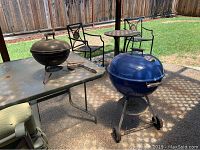 Photo of large blue BBQ pit, mini black BBQ pit, and BBQ tools on table in backyard setting