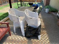 Stack of 10 white plastic patio chairs, stacked and secured with black tape, showing the side profile and armrests of the chairs