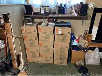 12 closed cardboard Home Depot moving boxes stacked under a shelf with stereo components and water bottles on top