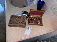 Wider shot of two wooden jewelry boxes and Philips Norelco electric shaver on tiled counter, items untested with some wear.