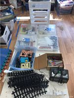 Overview photo showing multiple plastic storage containers, train tracks on table, boxed train parts, and electrical train controllers