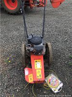 Full front view of red Bear Cat brush trimmer on gravel with tractor behind and spool of yellow trimmer line beside deck