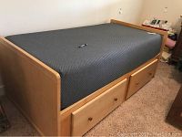 Light wood twin bed frame with two underbed drawers and grey quilted pad in place