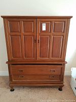 Front view of teak wardrobe showing double paneled doors upper cabinet, two large drawers below, and unique rounded feet.