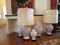 Two white lace ceramic table lamps with fabric shades, two matching ginger jars with lids, and a side table on wooden bases shown as full group from front