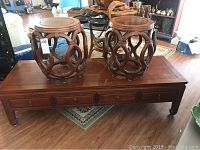 Overview of the rosewood coffee table featuring five drawers and two matching stools with circular tops and openwork design on sides.