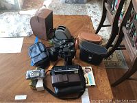 Full lot display on table showing binoculars, projector, camera, and carrying cases.