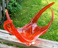 Side view of mid-century modern electric orange abstract glass bowl with whiplash form on an outdoor wooden surface