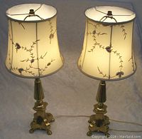 Pair of gilt metal lamps illuminated to show texture and embroidery on fabric shades, with cords visible.