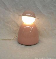 Front view of the pink robot lamp with light on. Shows the round glowing head with a flat circular hat and wide tapered base.