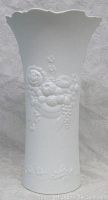 Front view of white porcelain vase showing embossed floral pattern and scalloped top edge.
